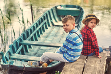 Brother and sister on a walk in the countryside . Children at the river with boats .