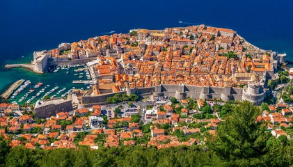 Fototapeta na wymiar A high angle view of the entire Old Town of Dubrovnik, Croatia, with its terracotta rooftops, surrounded by stone walls and a small boat harbor open to the Adriatic Sea.