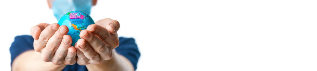 Banner. Close-up of a man's hands holding a globe, with images of North America: USA and Canada,  a man in a  mask out of focus, dressed in a blue t-shirt, uniform on a white background. Coronavirus