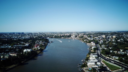 A photo of the Brisbane river with the suburb of East Brisbane on the right and the suburb of New Farm on the left. With a CityCat coming down the middle of the river.