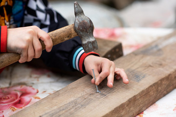 the boy’s hands are holding a hammer and hammering a nail into the board. The child repairs 