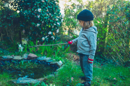 Little preschooler with stick by pond