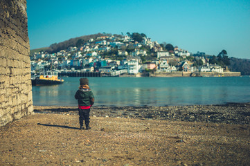 Little preschooler standing by the water in seaside town