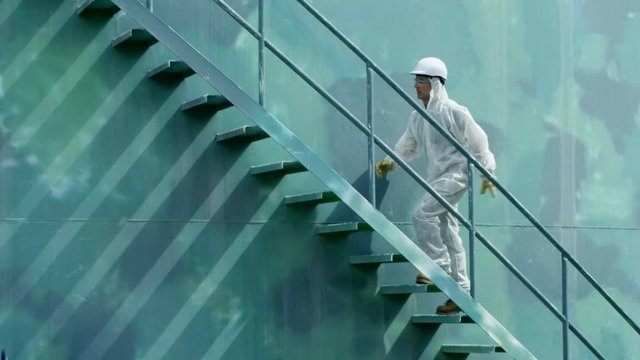 WS TS Worker in protective coverall ascending stairs on storage tank
