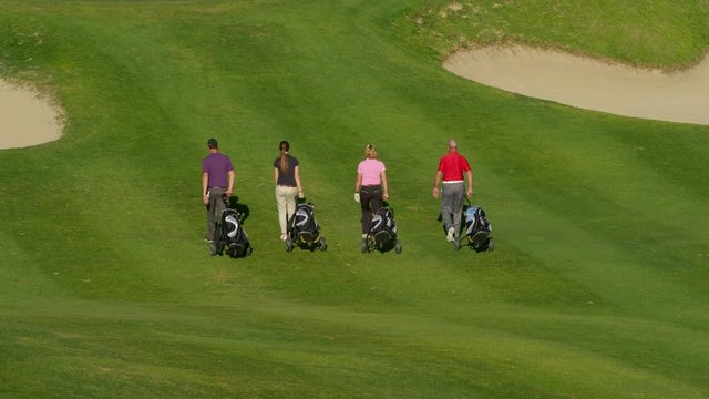 WS TS Four golfers with golf bags walking towards putting green