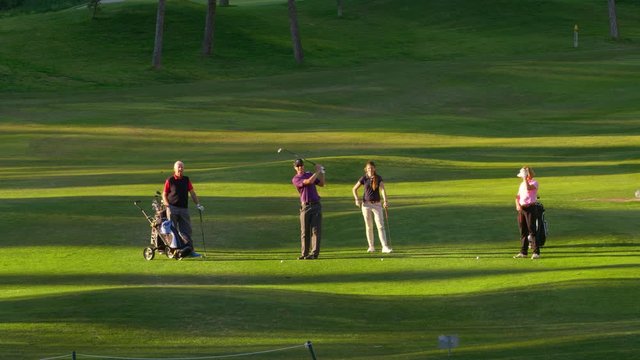 WS Four golfers on fairway, young man playing ball towards camera