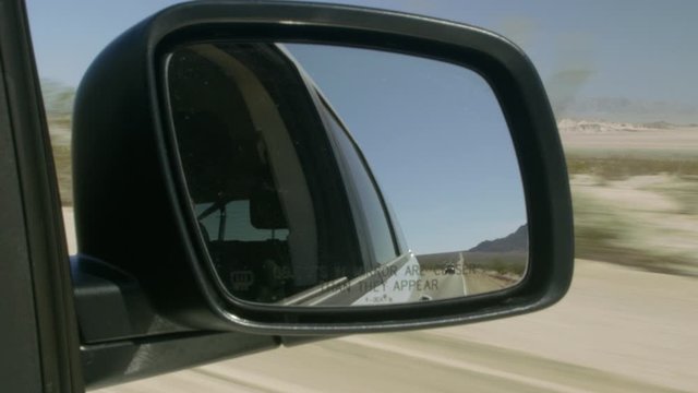 POV View Through Side View Mirror Of Car Driving Through Desert