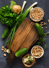 Vegan Menu Concept. Wooden rustic cutting board with ingredients for cooking vegan food on dark background top view