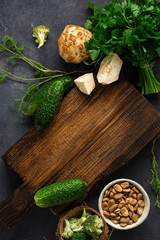 Menu food background. Rustic wooden cutting board with ingredients for cooking vegan food on dark background top view