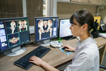 Asian Radiologist interpreting CT image with blur Hip Computed Tomography Volume Rendering technique(VRT) background.
