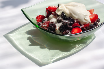 Strawberries, raisins and cottage cheese with sour cream in a green glass plate on a white background. Beautiful shadow from the plate. Healthy breakfast. Horizontal.