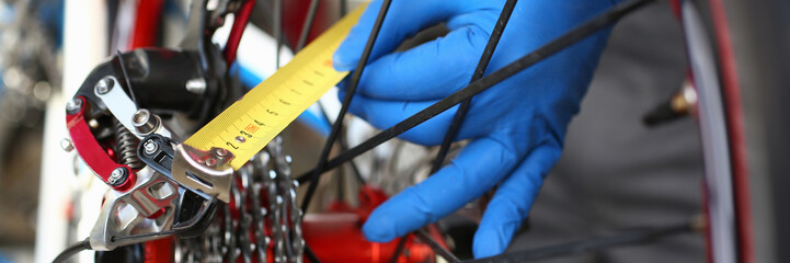 Close-up of male hands using measure tape for problem identification. Skilled mechanic working in bicycle repair shop service. Technical expertise concept - obrazy, fototapety, plakaty