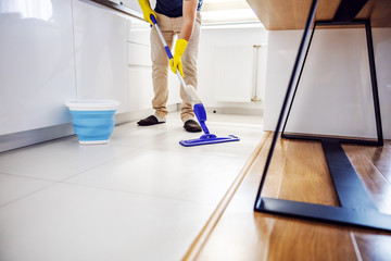 Young worthy man cleaning kitchen floor and trying out new cleaning product.