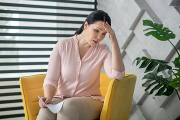 Woman in pink blouse and trousers sitting in an armchair.
