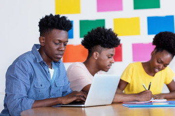 Young african american male student at computer with group of students