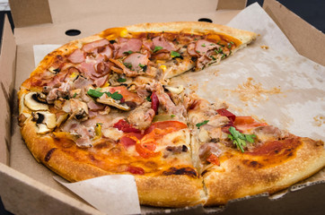 tasty pizza in a box on a black background. Close-up. Pizza with ham, meat, cheese, tomatoes and crab. There are no two pieces.