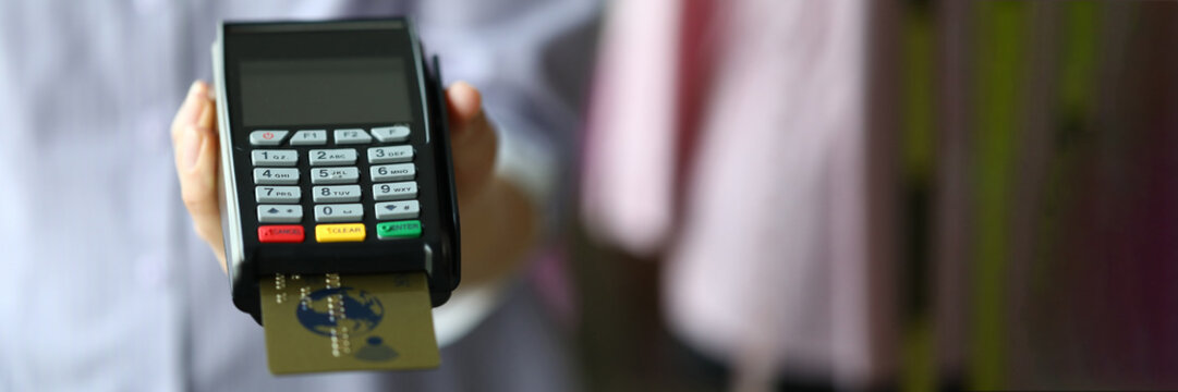 Woman hand hold POS termimal with gold plastic debit card closeup background.
