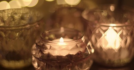 Cluster of tea lights in glass holders is lit with a lighter, with bokeh in background.
