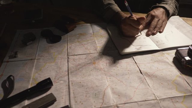 Man drawing map on his rustic table with camping accessories