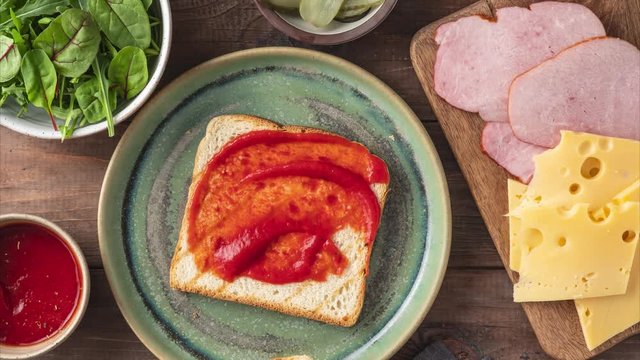 Sandwich with cheese, ham, tomato sauce, с bread, the process of making sandwiches with various fillings on a wooden background, top view, 4k, motion stop animation