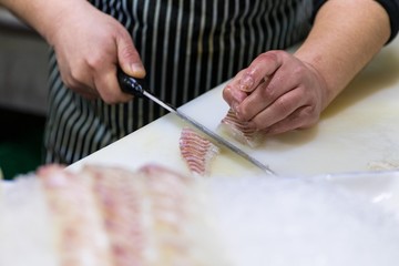 Chef cutting a fresh slices of salmon sashimi with a sharp knife. Japanese traditional seafood restaurant.