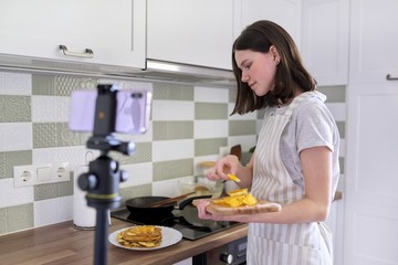Teenager girl, food blogger cooking pancakes with orange at home in kitchen
