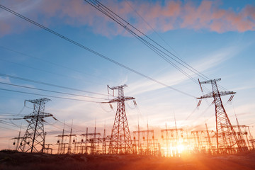 Electric network of pylons against a cloudy sky and a green meadow