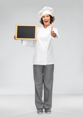 cooking, advertisement and people concept - happy smiling female chef holding black chalkboard showing thumbs up over grey background