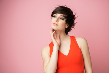 Beautiful young female posing at studio over pink background wearing vivid orange summer dress. Portrait of pretty happy brunette woman looking at copyspace
