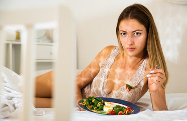 Portrait of lady eating vegetable salad in bed at home alone