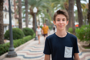 Handsome young boy looking at camera over promenade of Alicante. Beautiful calm smiling teen boy at...