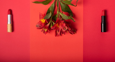Creative beauty  concept of two red lipsticks and red flowers on a red and bright pink background....