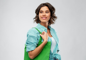 people concept - portrait of happy smiling young woman in turquoise shirt with green reusable canvas bag for food shopping on grey background