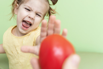 Fototapeta na wymiar a little girl emotionally refuses the proposed tomato. children do not like vegetables, unbalanced nutrition of preschoolers