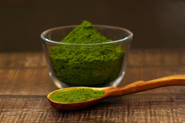 Green tea matcha in a glass bowl and a spoon on a brown wooden background close-up. Matcha in a wooden spoon.
