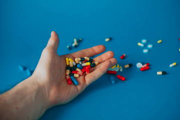 a bunch of different pills in a man's hand on a blue background