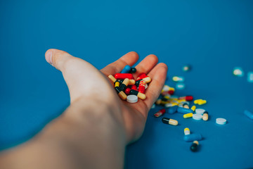 a bunch of different pills in a man's hand on a blue background