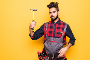 Young indian handyman with hammer in hands isolated on yellow background