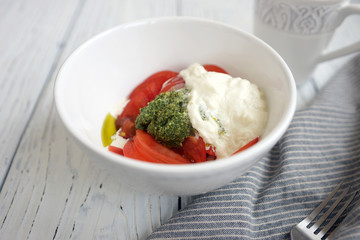 Tomatoes, pesto and stracciatella cheese in a white bowl in the background
