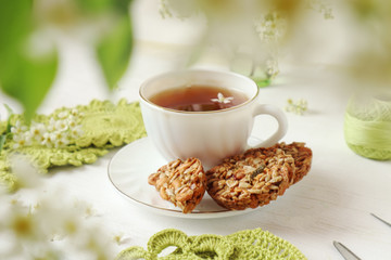 Time for a Cup of tea - a time of reflection and enjoyment. White tea Cup with cookies and branches of cherry blossoms and needlework.