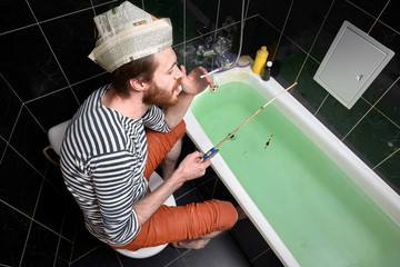 home isolation and quarantine concept. holiday at home, man catches fish in bath. newspaper cap with unreadable text