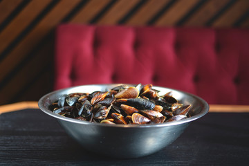 Shells clams with parsley in copper cooking dish on dark wooden table with blurred restaurant background.