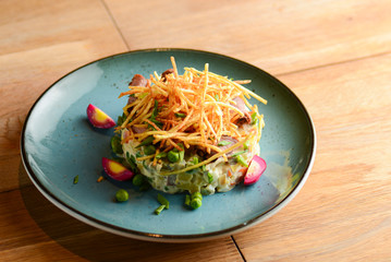 Traditional Russian salad Olivier served on a blue plate over light rustic wooden table.