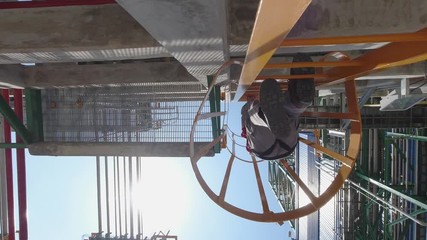 Engineers wear a full body safety harness and climb up the vertical ladder in an industrial factory to check the condition of the equipment.