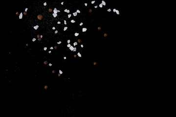 Levitating salt crystals and black pepper spice on black. Copy space