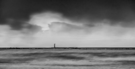 Sea waves of Baltic sea at long exposure. Cloudy sky over the water. Lonely lighthose. Black and white.