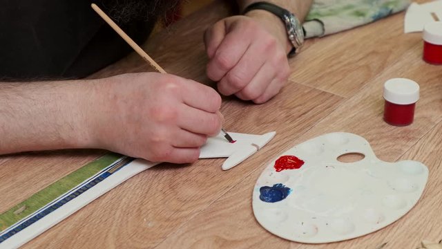 mature man paints tail unit of passenger jetliner model sitting at table in Sunday school class closeup slow motion