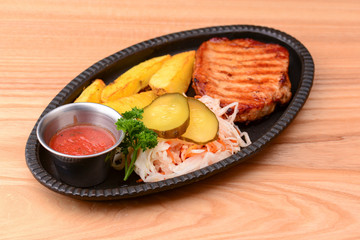 Grilled steak with vegetables and tomato sauce served on a black plate over light rustic background.