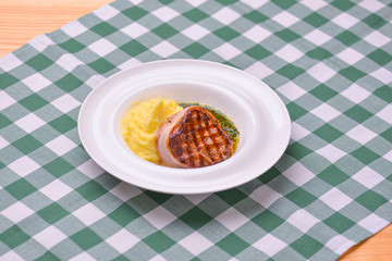 Filet mignon with mashed potatoes and pesto sauce served in a white plate over green plaid tablecloth. Beef steak.