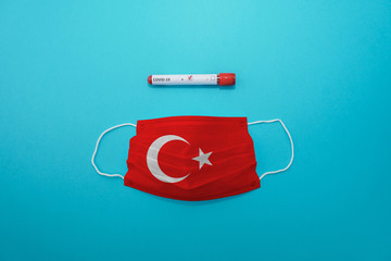 Disposable medical surgical face mask with Turkey flag superimposed on it with positive COVID-19 test on blue background. Coronavirus (COVID-19) pandemic affects the country. Stay home, stay safe